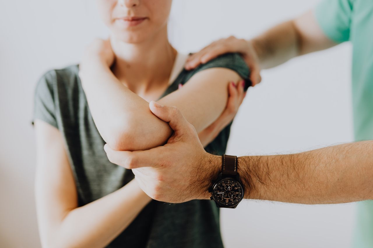about-01 Crop faceless osteopath in modern wristwatch and uniform bending arm of anonymous thoughtful woman in casual wear in doctor office in hospital